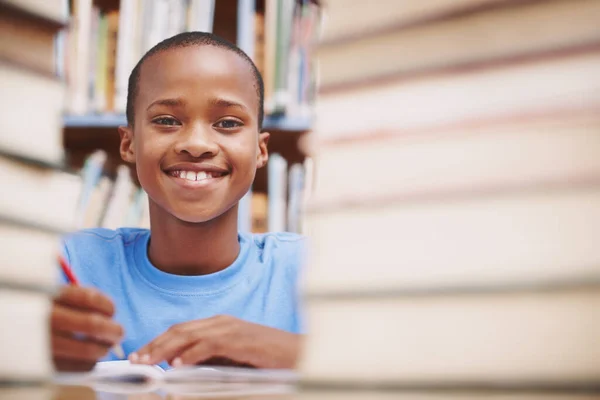 Hij houdt ervan om boeken te lezen. Een Afrikaans-Amerikaanse jongen omringd door boeken in de bibliotheek. — Stockfoto