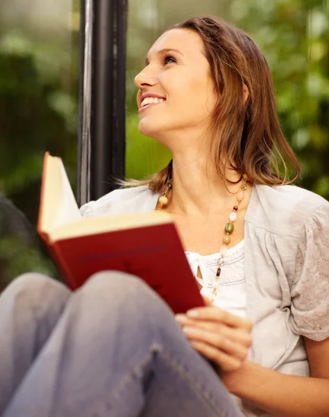 Non c'è niente di meglio che rilassarsi con un buon libro. Una bella donna che legge seduta accanto ad una finestra. — Foto Stock