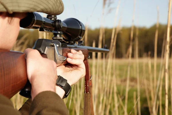 Patience is the secret to a perfect shot. A game hunter looking through the reeds with his sniper rifle. — Stock Photo, Image