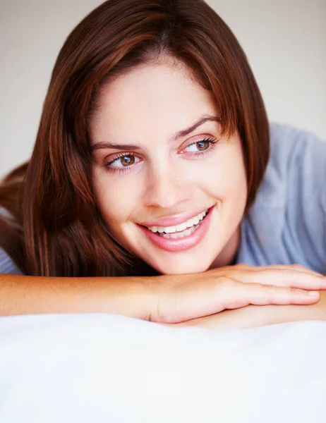 Sonriente linda morena femenina acostada en la cama. Primer plano retrato de una guapa morena sonriente acostada en la cama. —  Fotos de Stock