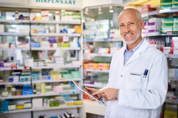 Segít egy hatékonyabb gyógyszertárat vezetni. Egy érett gyógyszerész portréja, aki digitális tablettát használ, miközben vegyésznél dolgozik. — Stock Fotó
