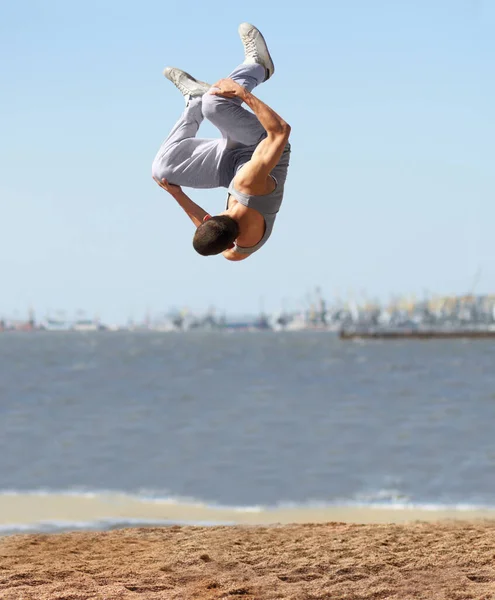 Ondersteboven en ondersteboven. Een atletische jongeman doet een salto op het strand.. — Stockfoto