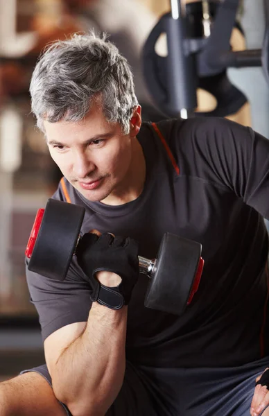 Definiendo sus bíceps. Un hombre maduro haciendo rizos de bíceps con una mancuerna en el gimnasio. —  Fotos de Stock