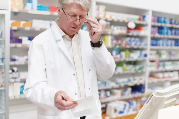 Gyógyszerész átnézi a receptet. Gyógyszerész portréja, amint receptre kapható a gyógyszertárban. — Stock Fotó