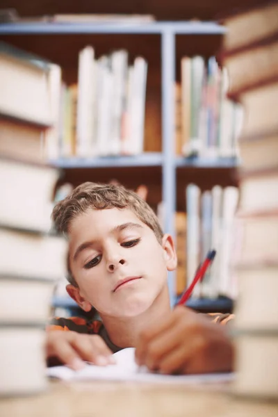 若い男の子が本の山の間で創造的な執筆をしてる. — ストック写真