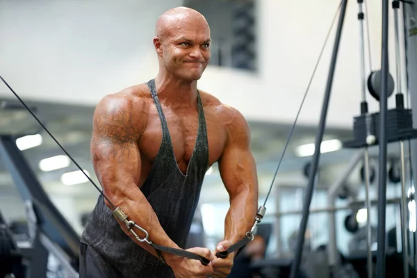 Jobbar hårt för att nå sina mål. En manlig kroppsbyggare som använder träningsutrustning för att träna på gymmet. — Stockfoto