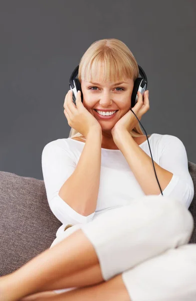 Een vrouw die naar een koptelefoon luistert. Gelukkige jonge vrouw zitten op de bank en luisteren naar muziek. — Stockfoto