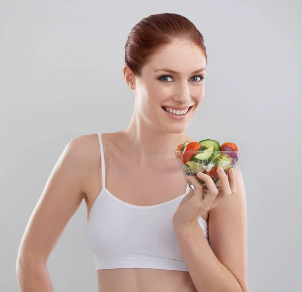 Njuter av hennes diet. Beskuren bild av en sportig ung kvinna i studion med en sallad. — Stockfoto