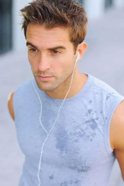 Hudba mi pomáhá cvičit. Detailní záběr pohledného mladého muže v propocené košili, jak poslouchá hudbu na sluchátkách. — Stock fotografie