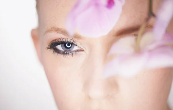 Visie van schoonheid. Een mooie jonge vrouw kijkt uit van achter een orchidee. — Stockfoto