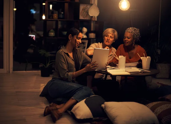 Cette application nous aidera à terminer la date limite. Tournage d'un groupe de femmes d'affaires travaillant ensemble sur une tablette numérique dans un bureau la nuit. — Photo
