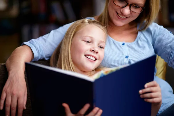 Czytanie ćwiczy mózg. Urocza młoda dziewczyna siedzi obok matki, gdy czytają książkę. — Zdjęcie stockowe