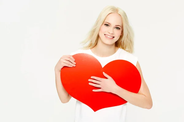 Glücklich und verliebt. Eine schöne junge Frau hält ein rotes Herz vor weißem Hintergrund. — Stockfoto