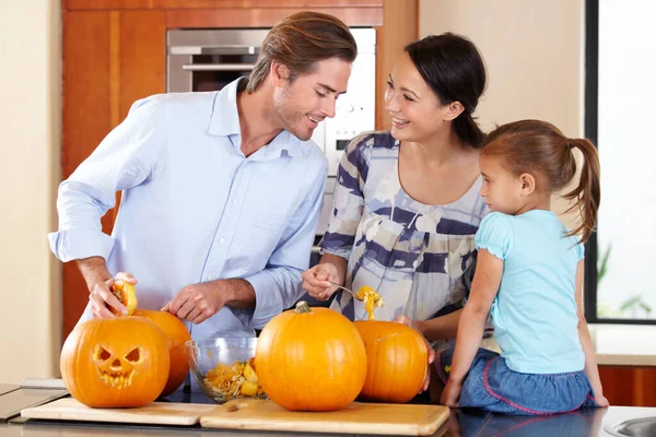 Ετοιμάζω την κολοκύθα για το Χάλογουιν. Μια νεαρή μητέρα και ο πατέρας στέκονται με τη μικρή τους κόρη σε μια κουζίνα ετοιμάζοντας Jack Olanterns για το Halloween. — Φωτογραφία Αρχείου