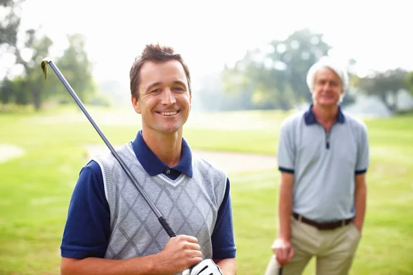 Αρσενικό γκόλφερ χαμογελάει. Πορτρέτο του ανθρώπου που κατέχει ένα μπαστούνι του γκολφ και χαμογελώντας με τον πατέρα στο παρασκήνιο. — Φωτογραφία Αρχείου