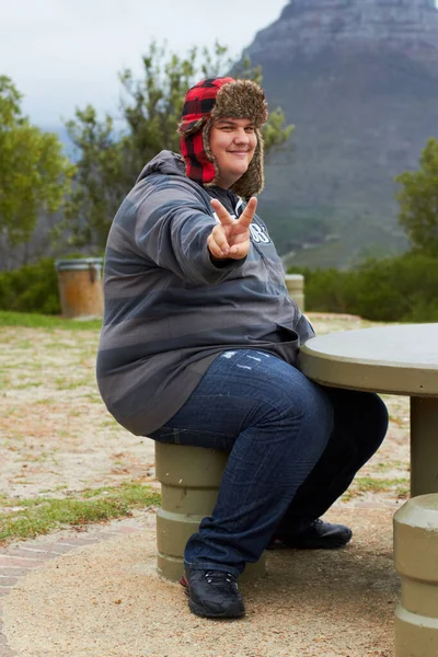 平和を。ピースサインを示すピクニックテーブルの外に座っている肥満の若い男. — ストック写真