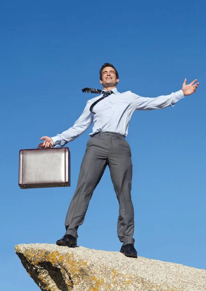 Non c'e 'limite a cio' che posso ottenere ora. Un giovane uomo d'affari euforico con una valigetta in piedi su una scogliera. — Foto Stock
