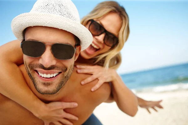 As melhores férias de sempre. Tiro de um jovem sorridente dando a sua namorada rindo um piggyback em uma praia ensolarada. — Fotografia de Stock