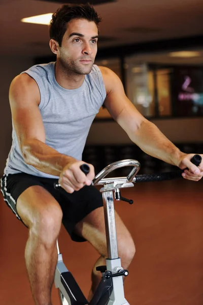 Πάει την ποδηλασία του σε άλλο επίπεδο. Ένας όμορφος νεαρός που φοράει αθλητικά ρούχα και χρησιμοποιεί ποδήλατο γυμναστικής στο γυμναστήριο.. — Φωτογραφία Αρχείου