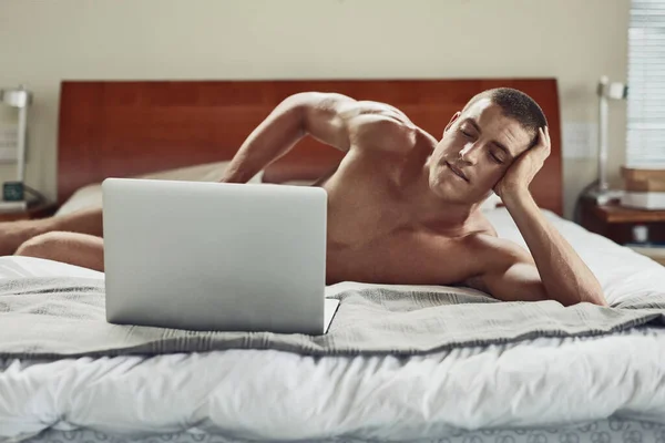 Preciso de uma namorada. Tiro de um jovem despreocupado nu deitado em sua cama enquanto estava ocupado com seu laptop em casa durante o dia. — Fotografia de Stock