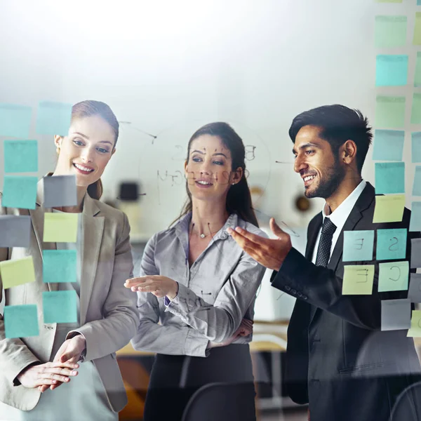 Putting ideas on paper. Shot of a group of businesspeople brainstorming on a glass wall with sticky notes in an office. — Stock Photo, Image