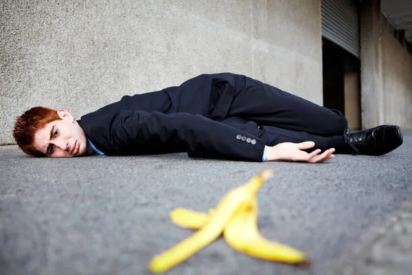A veces las pieles de plátano son inevitables. Un joven tirado en el suelo después de deslizarse sobre una cáscara de plátano. — Foto de Stock