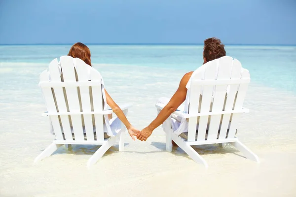 Λατρεύω το ζευγάρι που χαλαρώνει στις ξαπλώστρες. Οπίσθια όψη του αγαπημένου ζευγαριού κρατώντας τα χέρια, ενώ χαλαρώνοντας σε ξαπλώστρες στην παραλία. — Φωτογραφία Αρχείου