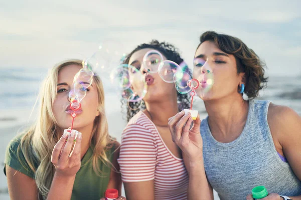 Blås bort dina bekymmer. Beskuren bild av tre vänner blåser bubblor på stranden. — Stockfoto