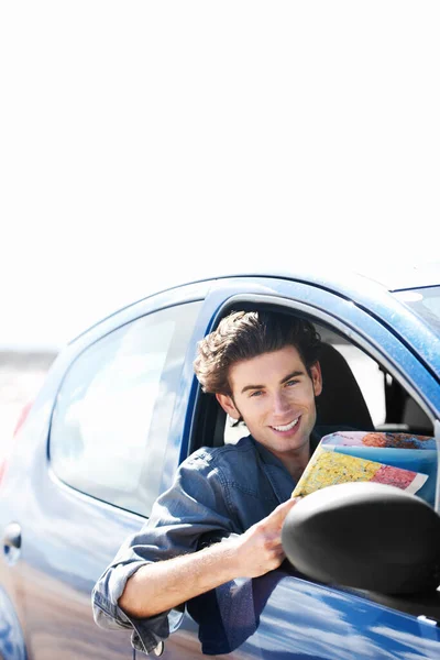 Ich bin auf dem richtigen Weg. Junger Mann sitzt im Auto und lächelt in die Kamera, während er eine Landkarte in der Hand hält. — Stockfoto