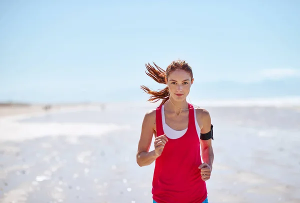 Determined to get fit. Cropped shot of a young woman running on the beach. — Stock Photo, Image