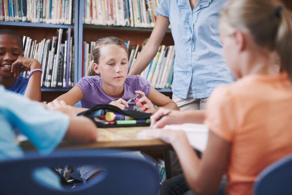 Concentreer je op haar werk. Een jong meisje zit in de bibliotheek met haar klasgenoten en lerares. — Stockfoto