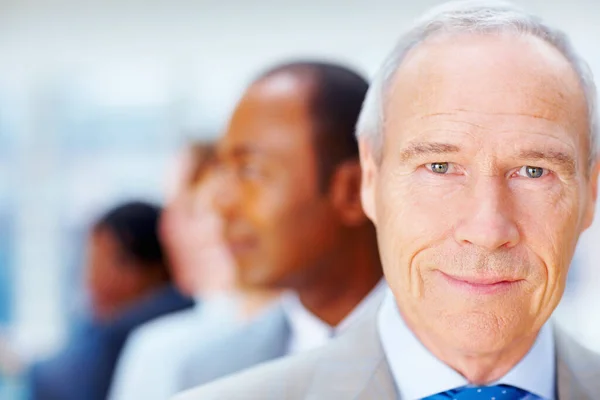 Un ejecutivo serio con equipo detrás de él. Primer plano del hombre de negocios senior con el equipo detrás de él. —  Fotos de Stock