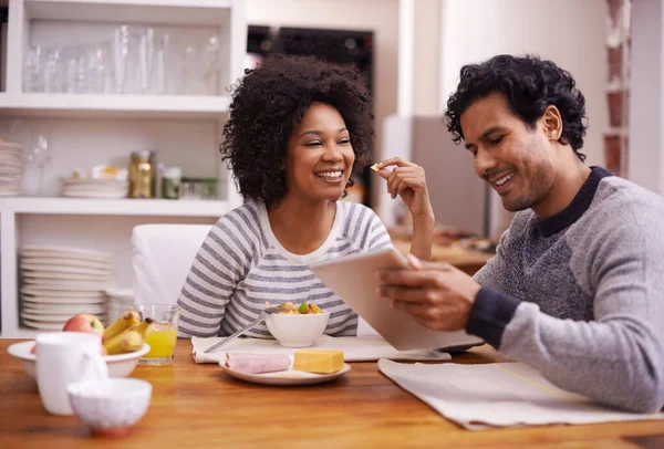 O dia é melhor quando começamos juntos. Tiro de um casal feliz desfrutando de café da manhã juntos enquanto procura um tablet digital. — Fotografia de Stock