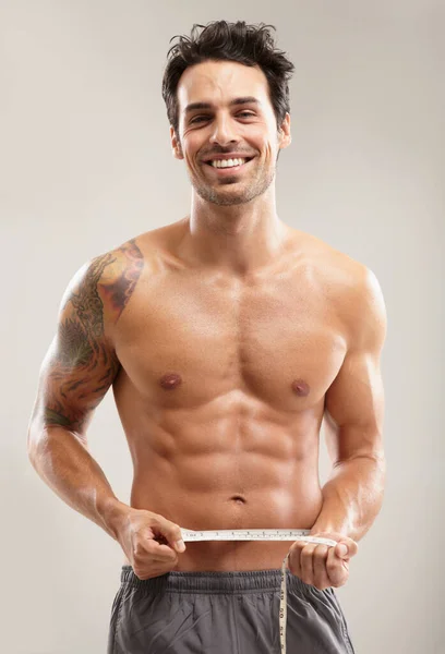Han mäter sina perfekta magmuskler. Porträtt av en stilig ung man som mäter sin midja. — Stockfoto