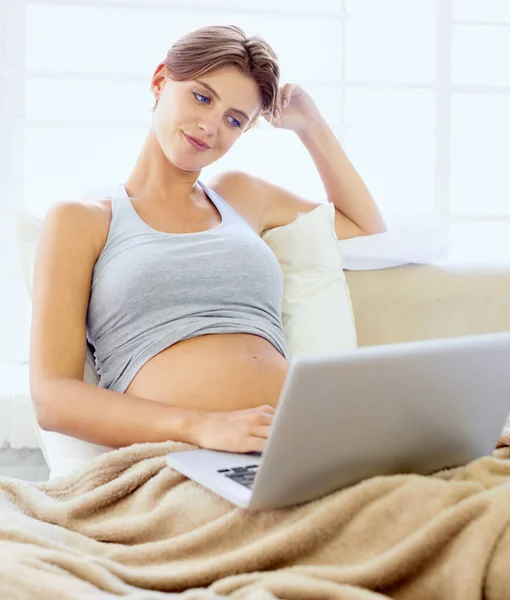 Zkoumání bohatství on-line informací o těhotenství. Krásná mladá těhotná žena sedí v posteli se svým notebookem. — Stock fotografie