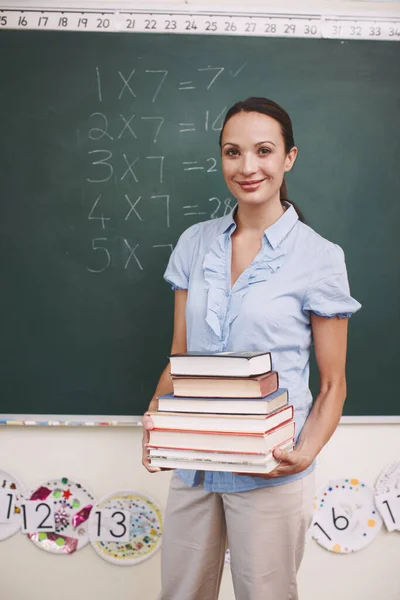 Vorbereitet auf eine spannende Lektion. Porträt einer hübschen Lehrerin, die einen großen Stapel Bücher in ihrem Klassenzimmer trägt. — Stockfoto