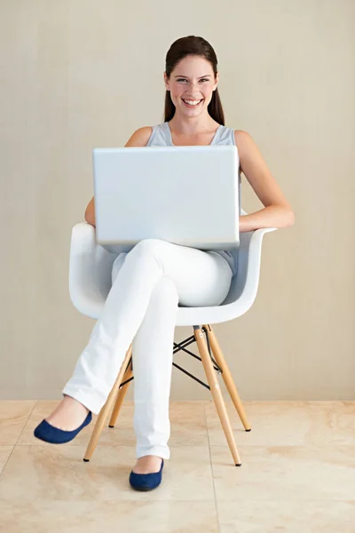 Δουλεύοντας από την άνεση του σπιτιού. Μια όμορφη νεαρή γυναίκα κάθεται σε μια καρέκλα και χρησιμοποιεί το laptop της. — Φωτογραφία Αρχείου