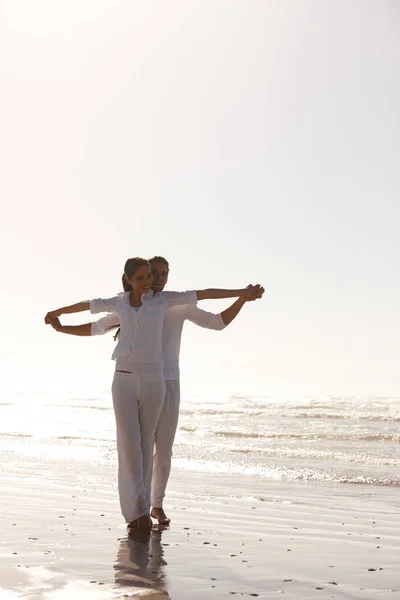 Rivelare la luce del mattino. Colpo a figura intera di una giovane coppia attraente vestita di bianco passeggiando lungo una spiaggia. — Foto Stock