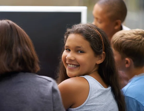 Улыбается во время компьютерных занятий. Портрет молодой школьницы, оглядывающейся назад во время работы за компьютером с друзьями. — стоковое фото