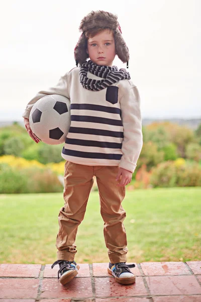Regen oder Sonnenschein. Aufnahme eines kleinen Jungen, der draußen mit seinem Fußball steht. — Stockfoto