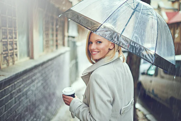 Aufwärmen mit einem Kaffee. Rückseite Porträt einer attraktiven jungen Frau, die mit Regenschirm und Kaffee im Regen spaziert. — Stockfoto