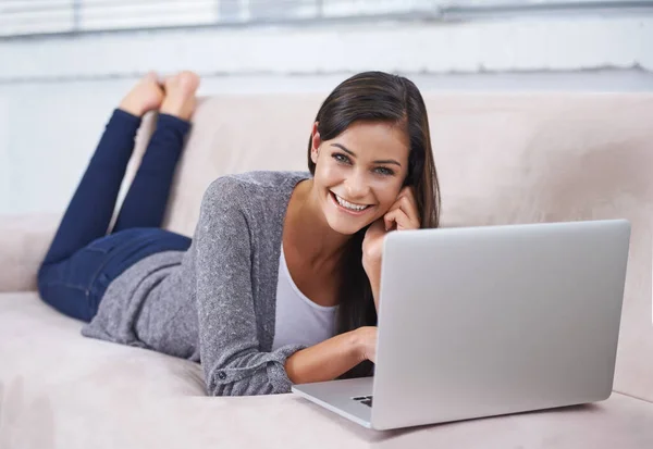 Online e al telefono. Una giovane donna si rilassa sul divano con un computer portatile e un cellulare. — Foto Stock