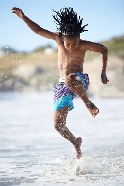 Una spruzzata. Un giovane ragazzo eccitato che salta in aria mentre è in spiaggia. — Foto Stock