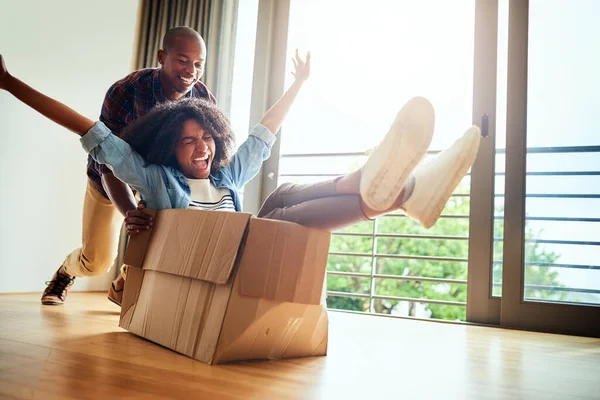 We all are still children deep inside. Shot of a cheerful young woman inside of a cardboard box being pushed by her boyfriend at home during the day. — Stock Photo, Image