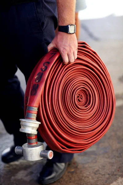 Enrolado e pronto para a ação. Tiro de perto de um bombeiro carregando uma mangueira de incêndio enrolada. — Fotografia de Stock