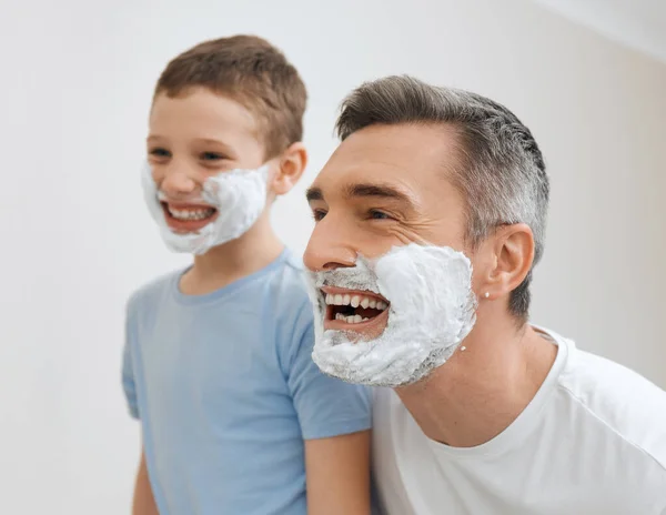 谁说学习不好玩的？一个英俊而成熟的男人在家里教他的小儿子如何在浴室刮胡子的剪下来的照片. — 图库照片