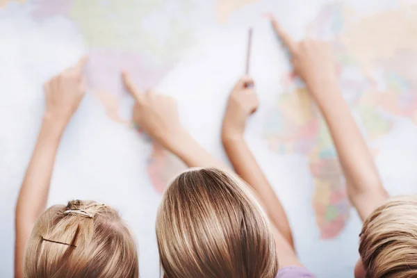 Есть так много мест, чтобы посетить. Вид сзади на группу школьников, указывающих на карту мира. — стоковое фото