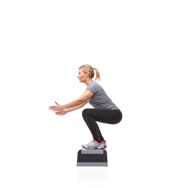 Facendo squat per tonificare il suo corpo. Una giovane donna sorridente che fa aerobica su un gradino aerobico su uno sfondo bianco. — Foto Stock