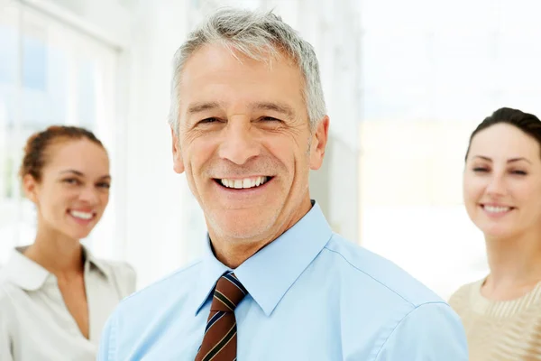 Leende affärsman med kollegor där bak. Porträtt av leende senior affärsman med kollegor i bakgrunden. — Stockfoto