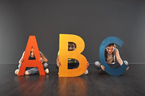 Wo Alphabetisierung beginnt. Studioporträt einer vielfältigen Gruppe von Kindern, die Buchstaben des Alphabets vor grauem Hintergrund hochhalten. — Stockfoto